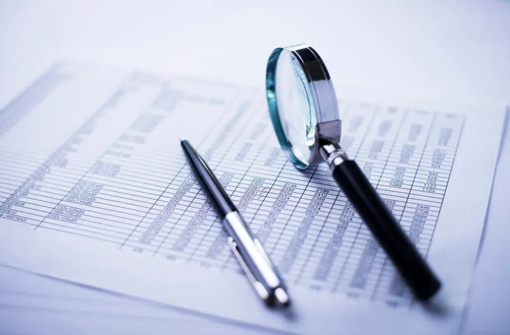 Magnifying glass over a printed financial spreadsheet with rows of numbers and data.