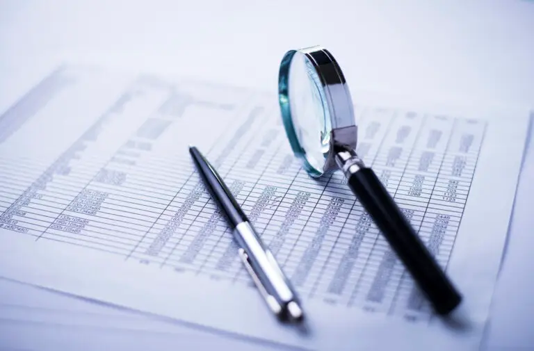 Magnifying glass over a printed financial spreadsheet with rows of numbers and data.